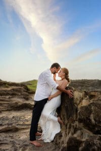 A loving couple embraces on a Maui beach during a romantic sunset photoshoot, with golden sand, gentle waves, and a breathtaking sky creating a dreamy atmosphere.