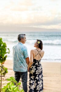 A loving couple embraces on a Maui beach during a romantic sunset photoshoot, with golden sand, gentle waves, and a breathtaking sky creating a dreamy atmosphere.