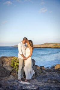 A loving couple embraces on a Maui beach during a romantic sunset photoshoot, with golden sand, gentle waves, and a breathtaking sky creating a dreamy atmosphere.