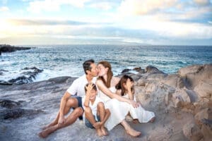 Family of four posing for a portrait on Maui Beach at sunset, smiling and embracing.