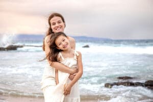 mother sharing a loving moment with her daughter as waves gently roll in behind them.